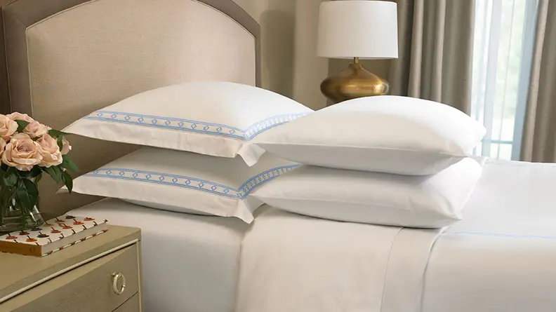 The best bed sheets for luxury, Frette for Ritz-Carlton bed sheets are shown in white with blue detailing.