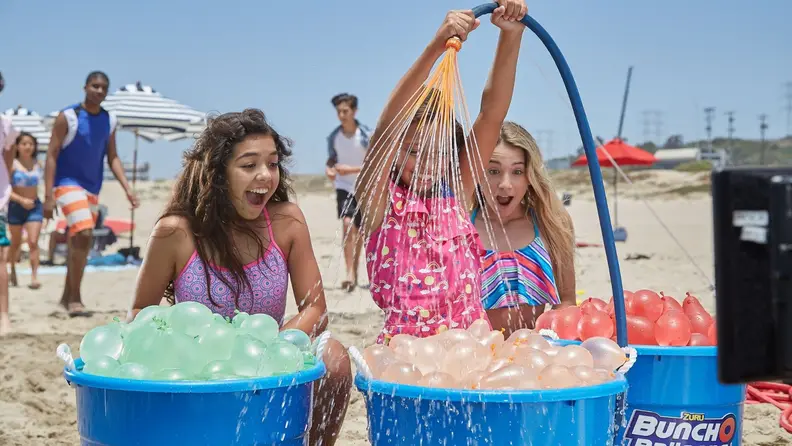 Three girls look on with excitement on buckets filled with full water balloons