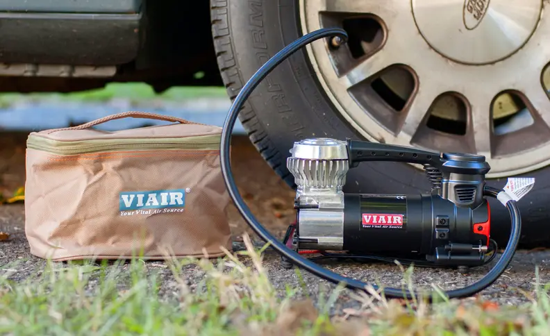 A Viair 85P portable air compressor is being used to inflate a car tire.