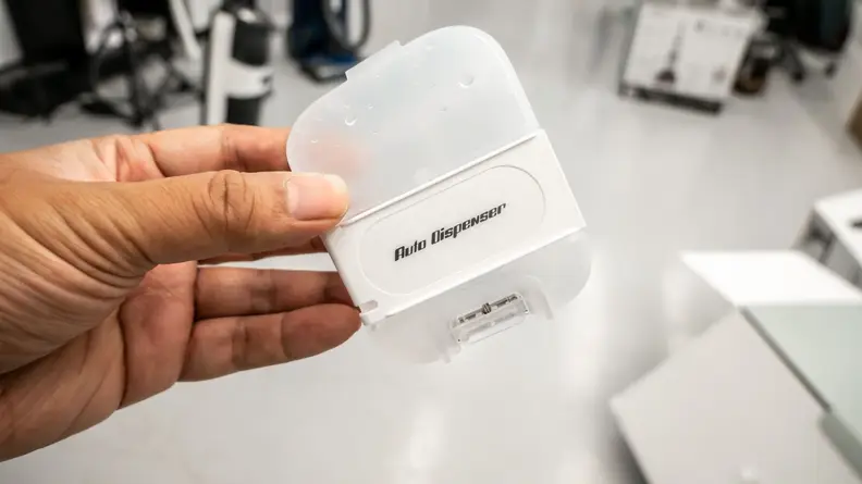 A left hand holds a small white box that is labeled auto dispenser.