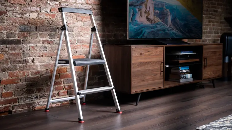 A step stool stands by a TV in front of a brick wall