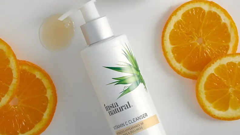 The InstaNatural Vitamin C Cleanser on a white background with orange slices surrounding it and a dollop of product pooling below the pump.