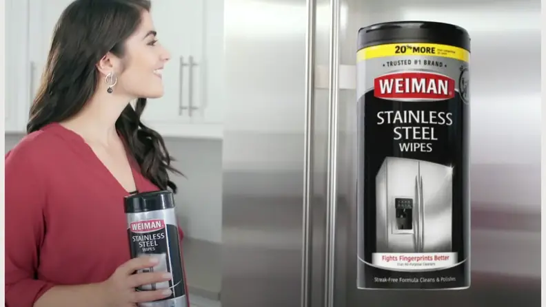 A lady holding a Weiman Stainless Steel Cleaning Wipes canister in front of a fridge, and a bigger image of the canister on the right