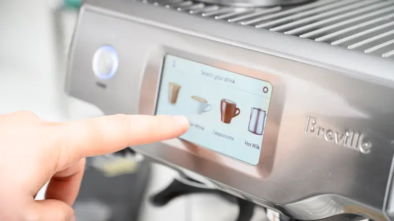 Hand touching an image of the LCD touchscreen on the Breville Barista Touch.
