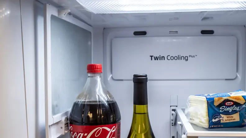 Image of one of the Samsung RF28R6301SR's flexible shelves in action. We see a coke bottle and wine bottle poking up from the bottom of the frame and off to the left a shelf is folded up, to allow both of them room to stand.