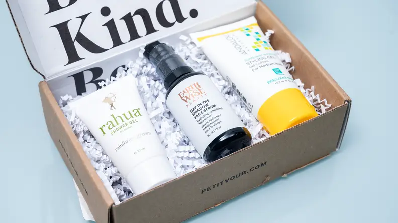 A small cardboard box containing three beauty products and paper confetti.