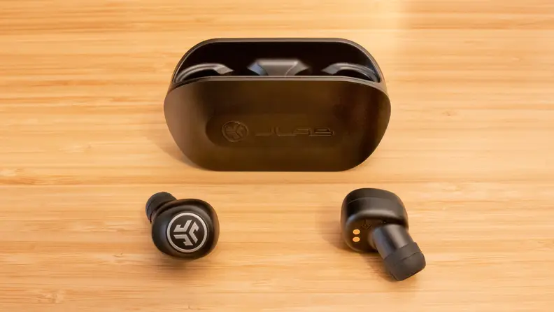 A pair of JLab Go Air earbuds and charging case on a brown table.