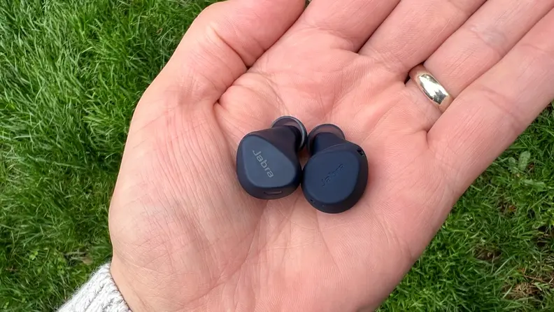 The navy Elite 4 Active and Elite 7 Active sit in an open hand before a grassy background.