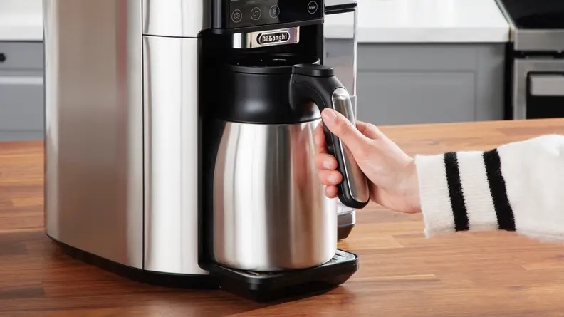 A person grabbing the De'Longhi TrueBrew carafe from the machine.