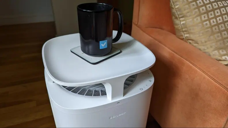 A coffee cup sits on top of an air purifier in a living room.