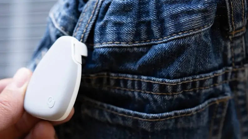 A white Jiobit tracker is attached to a belt loop on jeans.