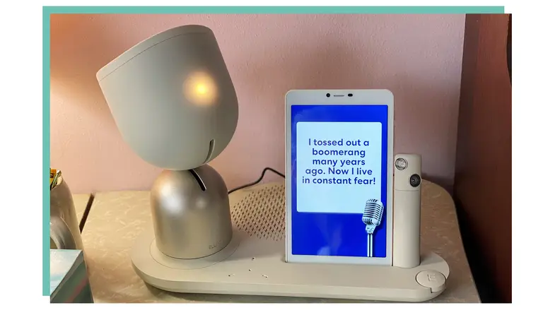 ElliQ robot displayed with a tablet with one of its interactive features, a joke that reads, "I tossed out a boomerang many years ago. Now I live in constant fear!"
