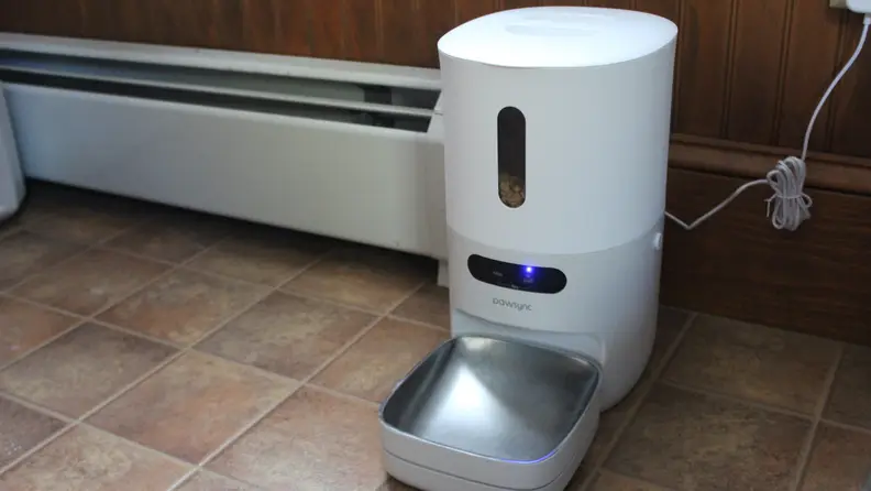 The PawSync Smart Pet Feeder on a tile floor plugged into a wall.