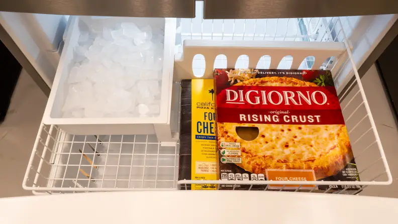 A freezer drawer is open; a couple frozen pizzas are stacked inside.