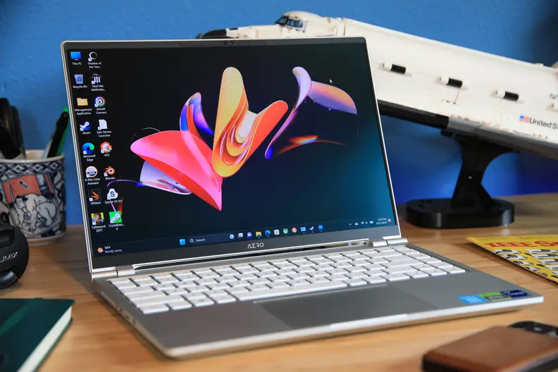 The Gigabyte Aero 14 OLED laptop open, with a design on the screen, surrounded by office supplies on a desktop.
