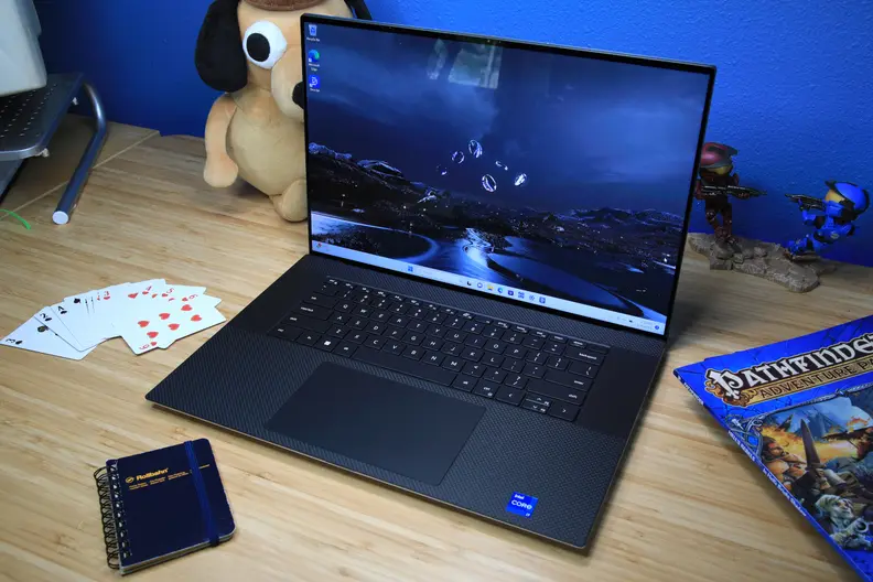 A laptop open and powered on flanked by knickknacks on top of a light brown wooden surface