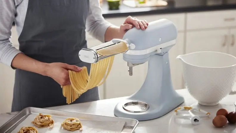 A hand making fresh linguine with a blue KitchenAid stand mixer.