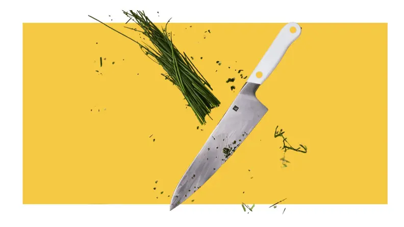 Chef's knife slicing through chives on a yellow background