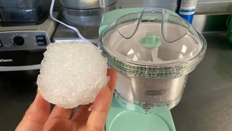 A person hold a ball of shaved ice in front of a small countertop shaved ice machine.