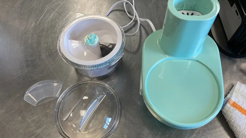 The parts of a shaved ice maker arranged on a stainless steel surface.