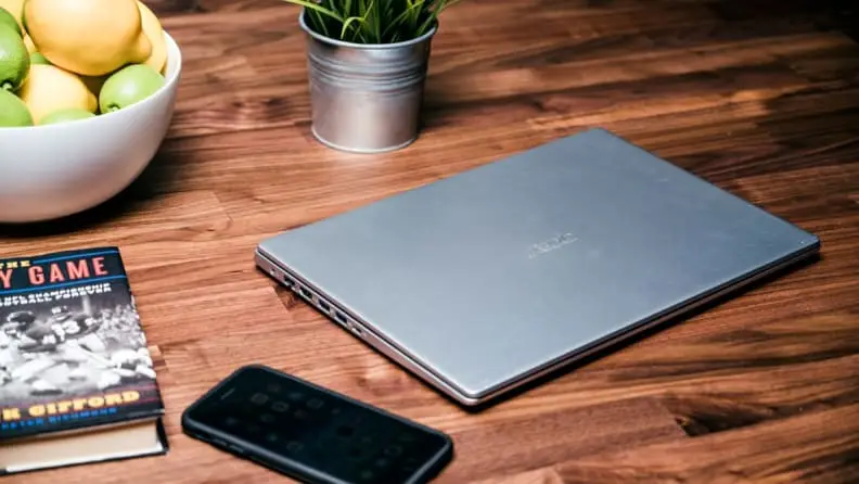 A closed laptop next to several items on wooden brown desk