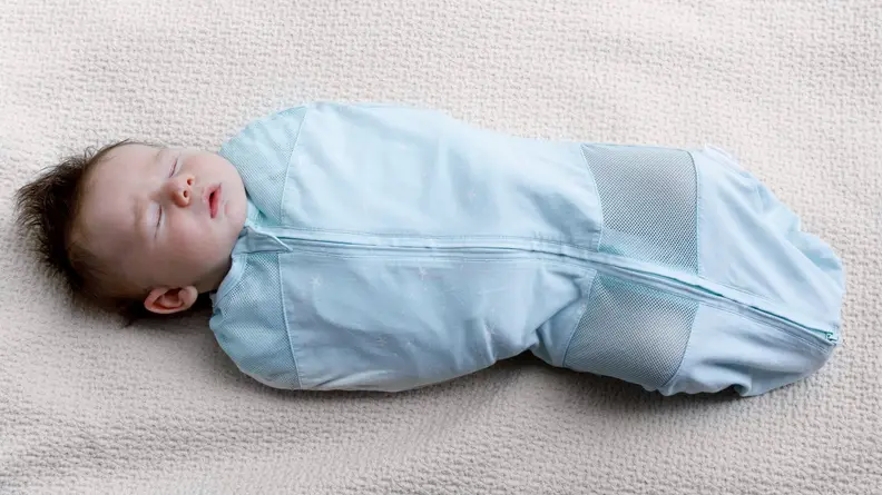 Sleeping dark haired baby wrapped in a blue Sleepea swaddle.