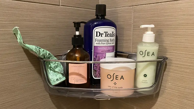 A corner shower caddy hangs in a tiled bathroom and is full of soap bottles