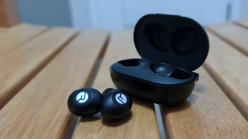 The all-black Raycon earbuds sitting out of their case on a slatted wooden bench.