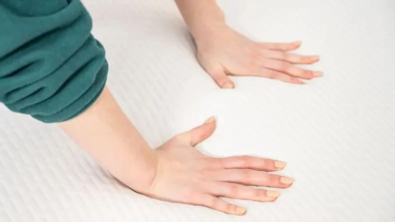 a woman's hands press into the surface of a foam mattress