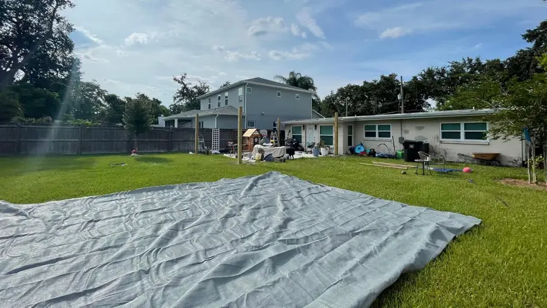 The shade sail laid flat on the backyard ground.