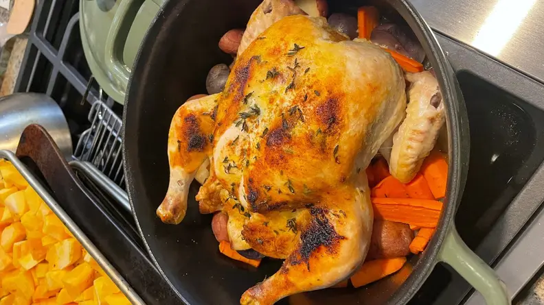 Roasted whole chicken surrounded by vegetables inside of dutch oven pot from Our Place.