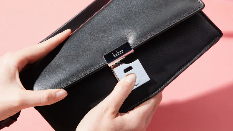 Two hands opening a Behno black leather handbag.