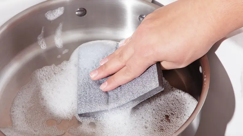 Person using Skura Style sponge to clean stainless steel pan in sink.