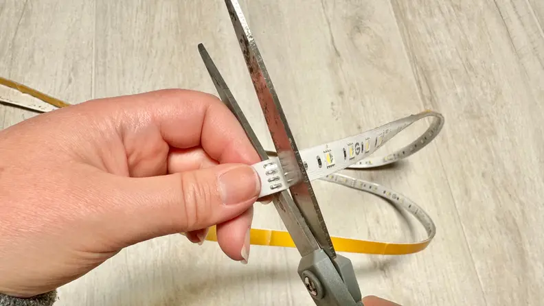 A pair of hands cutting the strip lights with a pair of scissors.