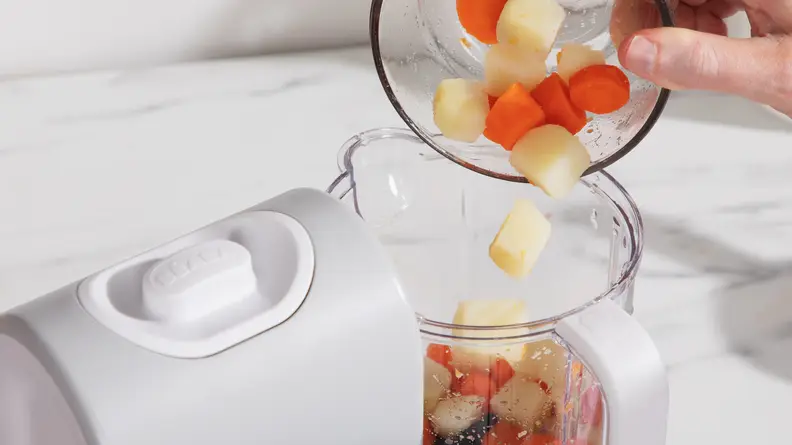 A hand putting chopped vegetables into the Beaba Babycook Express.