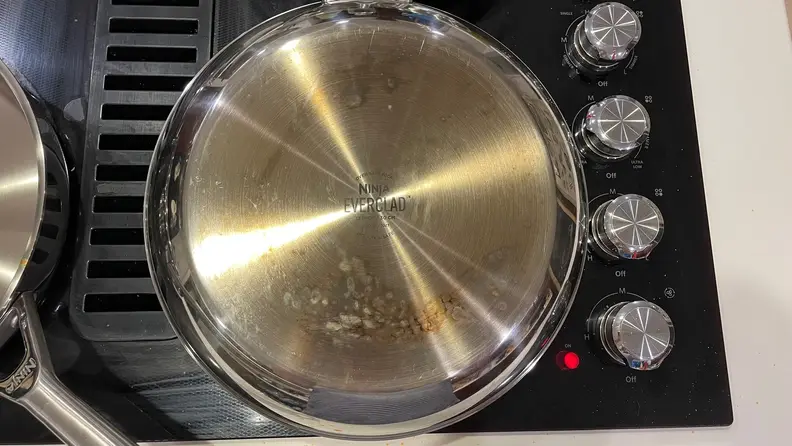 The bottom of a stainless-steel pan that's on a black stovetop.