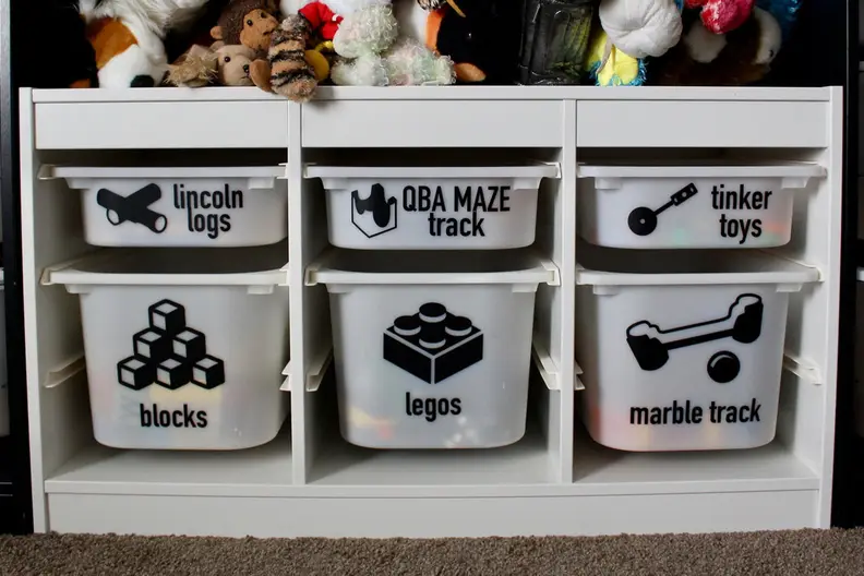 An organizer with six toy bins has each drawer labeled: Lincoln Logs, QBA Maze Track, Tinker Toys, blocks, Legos, marble track.