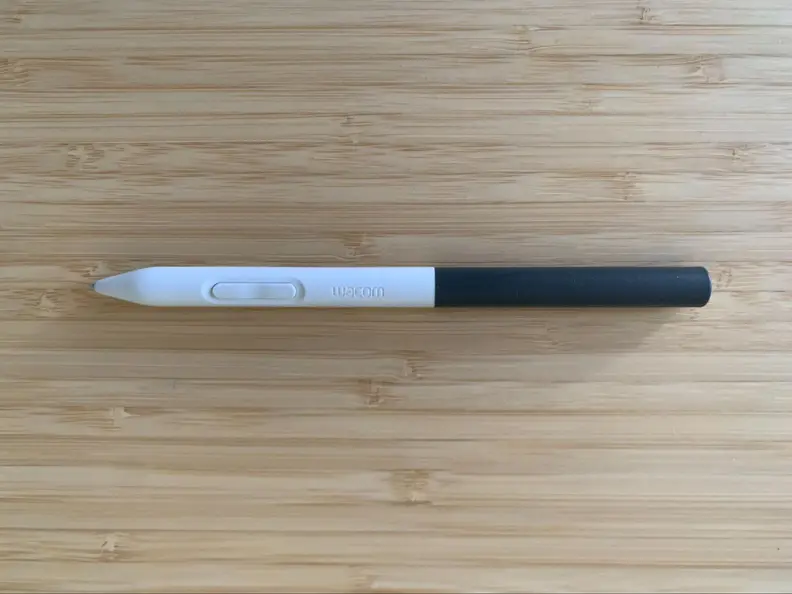 The white and gray Wacom digital drawing tablet pen appears on a bamboo desk, showing its button.
