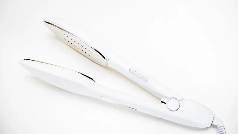 A travel iron that resembles a hair straightener rests on a surface