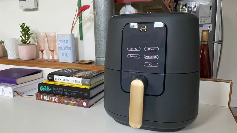 A black air fryer with a gold handle sitting on a white counter.