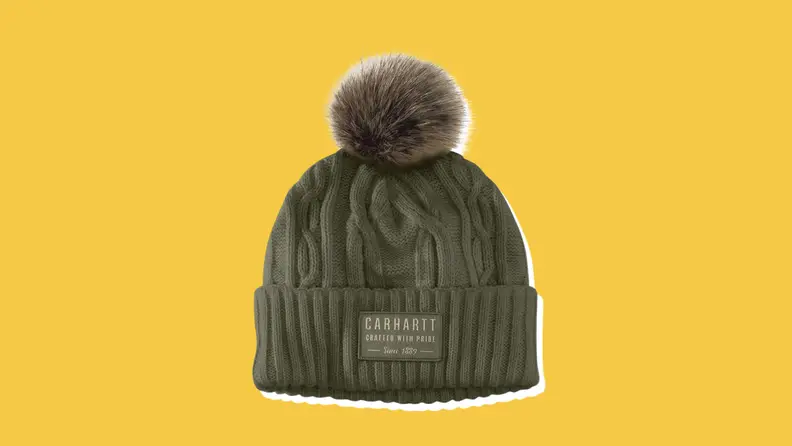 A dark green Carhartt Pom Beanie on a yellow background.