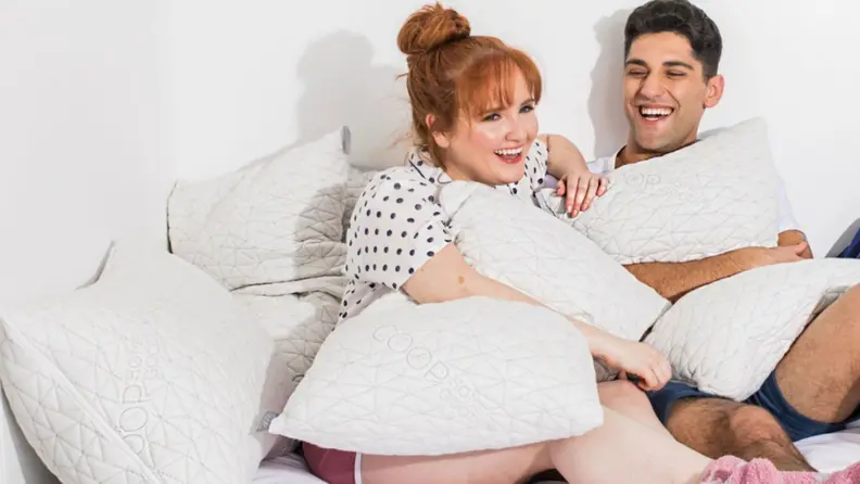 a couple with coop pillows surrounding them in bed