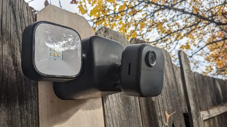 Lower view of the Blink Outdoor 4 Floodlight Camera mounted on wooden fence outdoors with two identical floodlights located on both sides.