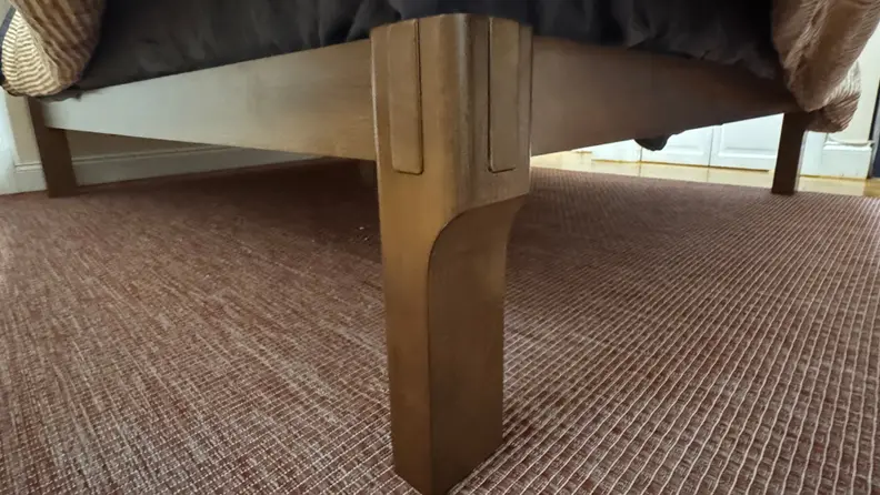 Corner of wooden FlexiSpot Kana bed frame showing the joinery assembled, on top of a marron and white rug.