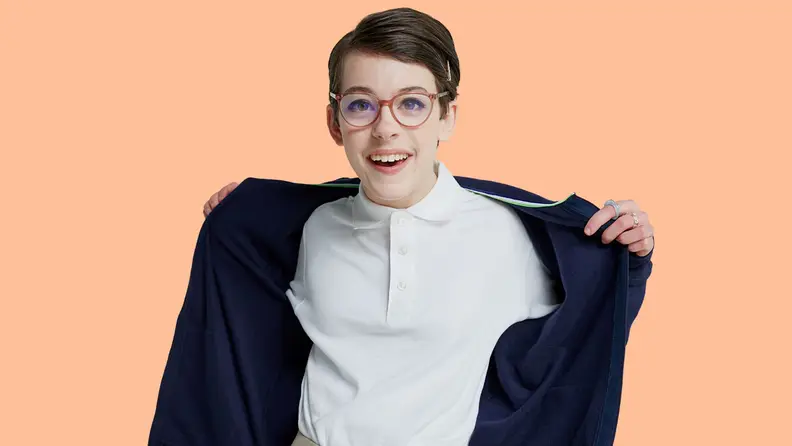 Young person in white polo smiling and putting on blue hoodie.
