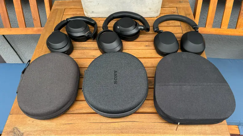 The Sony WH-1000XM4, Sony Ult Wear, and Sony WH-1000XM5 headphones and their cases next to one another on a wooden table.