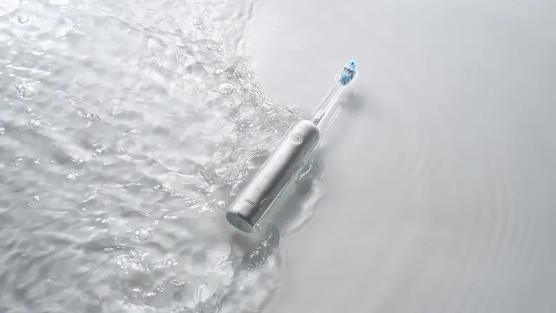 A sleek electric toothbrush lies partially submerged in rippling water, highlighting its water-resistant design against a clean, minimal background.