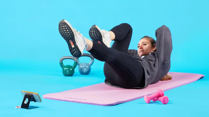 Person laying on yoga mat with feet elevated in the air and arms behind head completing a workout.