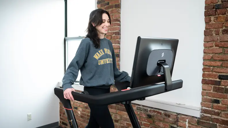woman wearing sweatshirt walking on peloton tread and laughing