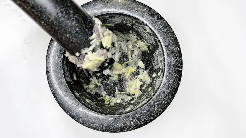 A person grinds alliums into a pulp using a mortar and pestle.
